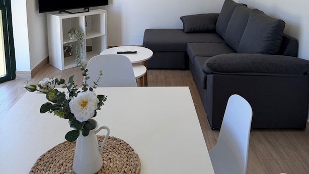 Un salon moderne avec un téléviseur à écran plat, un canapé gris, une table basse blanche et un tableau encadré accroché au mur.