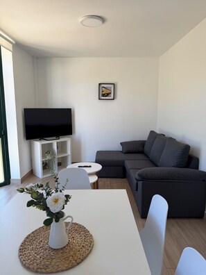 Una sala de estar moderna con un televisor de pantalla plana, un sofá gris, una mesa de centro blanca y un cuadro en la pared.