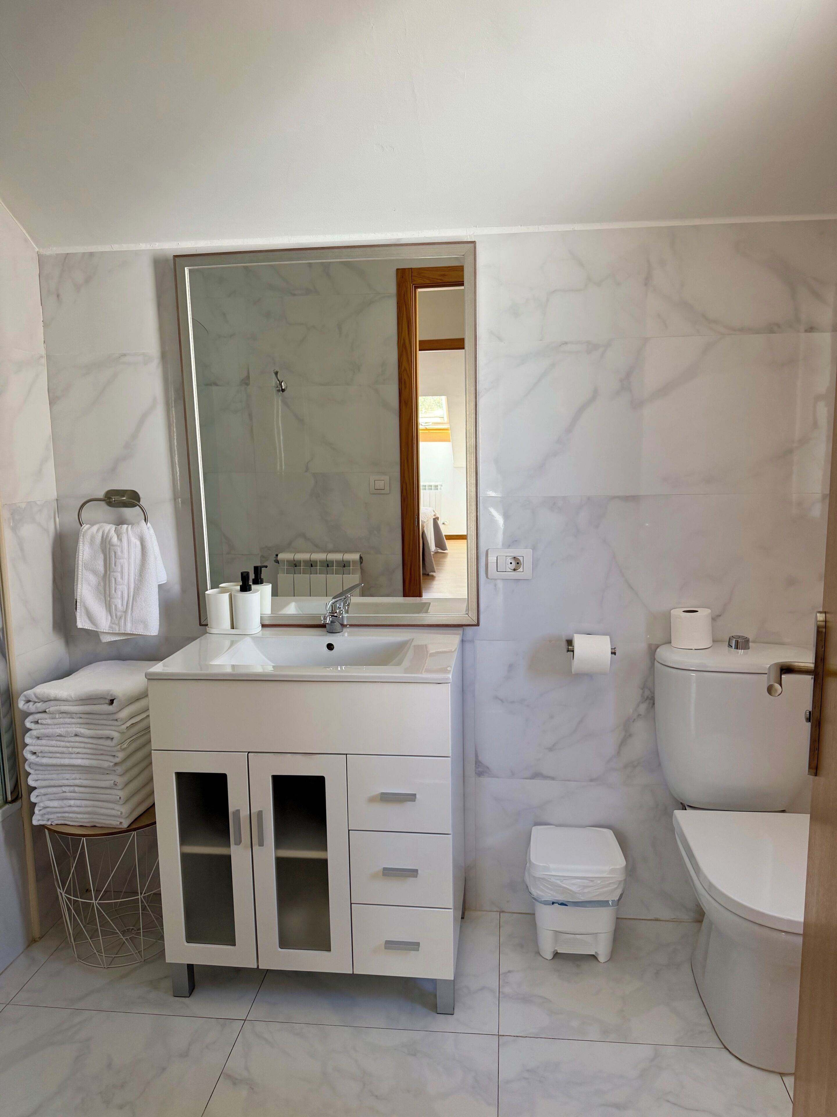 A modern bathroom with a white vanity, a large mirror, a toilet, and a sink.