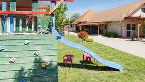 Ein Spielplatz mit Klettergriffen und einer Rutsche, neben einem Gebäude mit einem Ziegeldach und einer überdachten Terrasse.