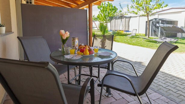 Eine Terrassengruppe im Freien mit einem runden Tisch, Stühlen und einem Frühstücksbuffet mit Früchten, Gebäck und Getränken.