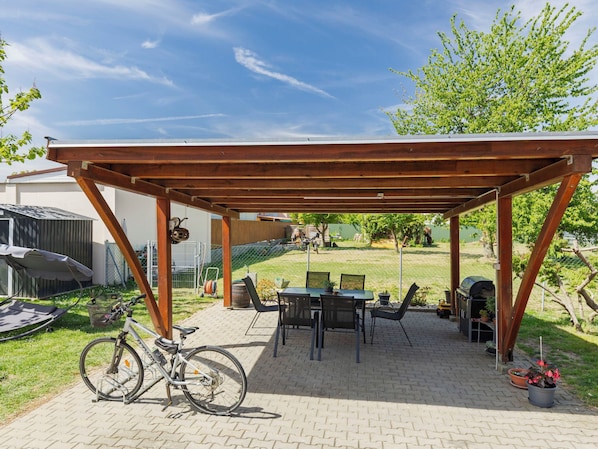 Ulkoterassi, jossa on puinen pergola, pöytä ja tuolit, polkupyörä ja grilli.