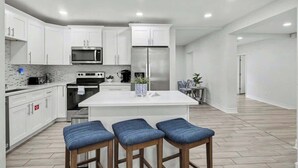 Una cocina moderna con armarios blancos, electrodomésticos de acero inoxidable y una isla central con taburetes de bar.
