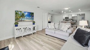 Una sala de estar con un sofá gris, un cuadro de una playa y una consola blanca con objetos decorativos.