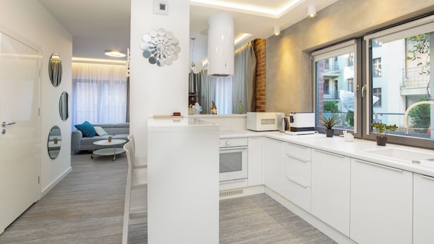 Une cuisine moderne avec des meubles blancs, un four à micro-ondes encastré et une grande fenêtre donnant sur la rue.