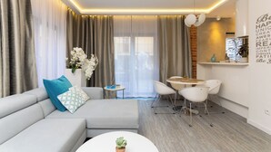 Un salon moderne avec un canapé gris, une petite table ronde et un coin repas avec des chaises blanches.