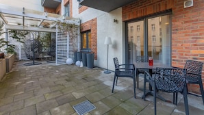 Un espace extérieur aménagé en terrasse, avec un mur en briques, une porte vitrée et une table entourée de chaises.