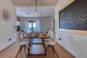 A dining area with a large table set for six, white chairs, pendant lights, and a chalkboard menu on the wall. - Villa La Vrana ZadarVillas (Vrana)