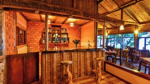 Eine rustikale Bar mit Holzstühlen, einer Backsteinwand und einem Strohdach.