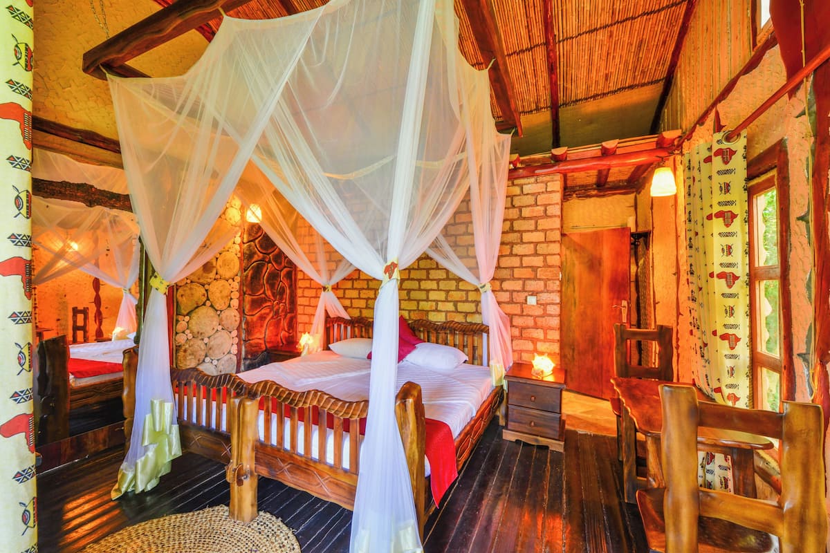 A room with a bed under a canopy, a wooden chair, and a brick wall.