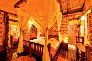 A room with a four-poster bed, a wooden bench, a table, and a brick wall. - Serenada Eco Resort  (Mukono)