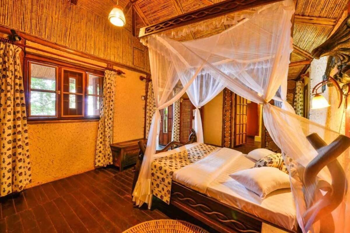 A room with a bed under a canopy, wooden floors, and a window with curtains.