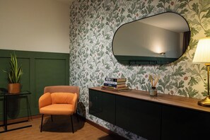 A room with a green wall, a large mirror, a wooden console table with books, a potted plant, and an orange chair. - Private Garden Flat, 2 Min walk to RED LINE M1, Direct to Duomo in 15 min (Milano)