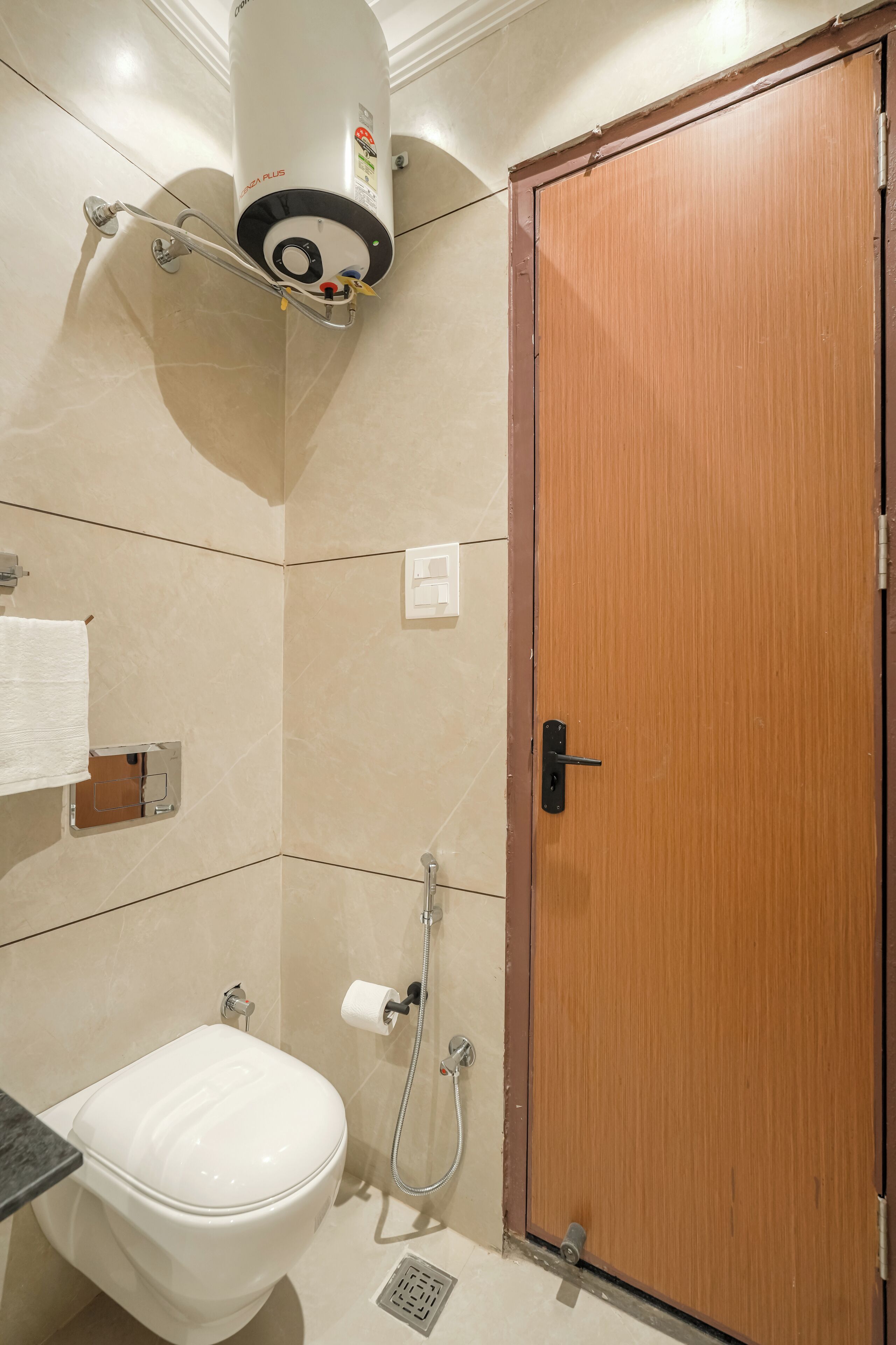 Un baño con inodoro, ducha, puerta de madera y un perchero para toallas.