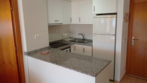 Eine kompakte Küche mit weißen Schränken, einem Edelstahl-Kühlschrank und einer Arbeitsplatte aus Granit.