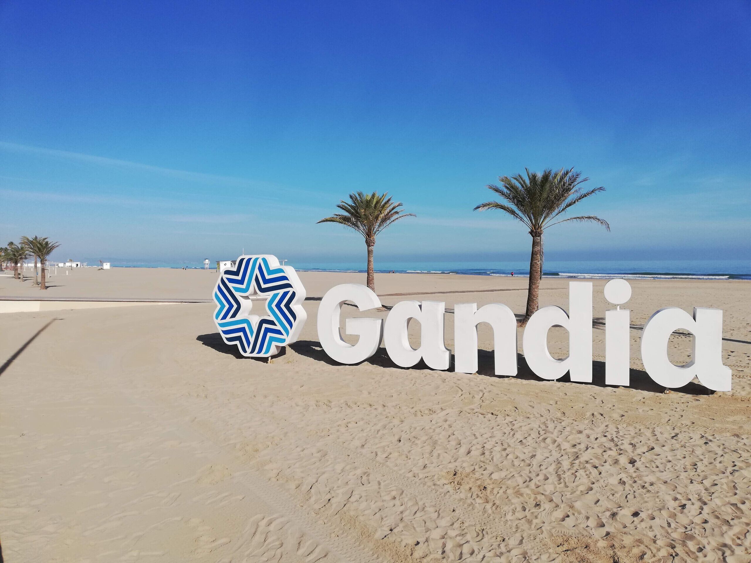 Una playa con el cartel 'Gandia' y palmeras.