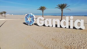 Ein Strand mit dem Schild 'Gandia' und Palmen.