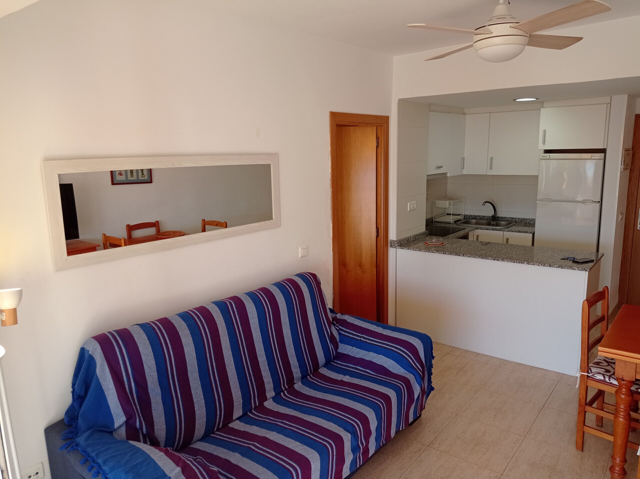 A compact living space with a sofa, a dining table, a kitchen area, and a ceiling fan.