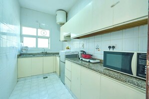 Une cuisine avec des armoires blanches, un four à micro-ondes, une cuisinière et une fenêtre.
