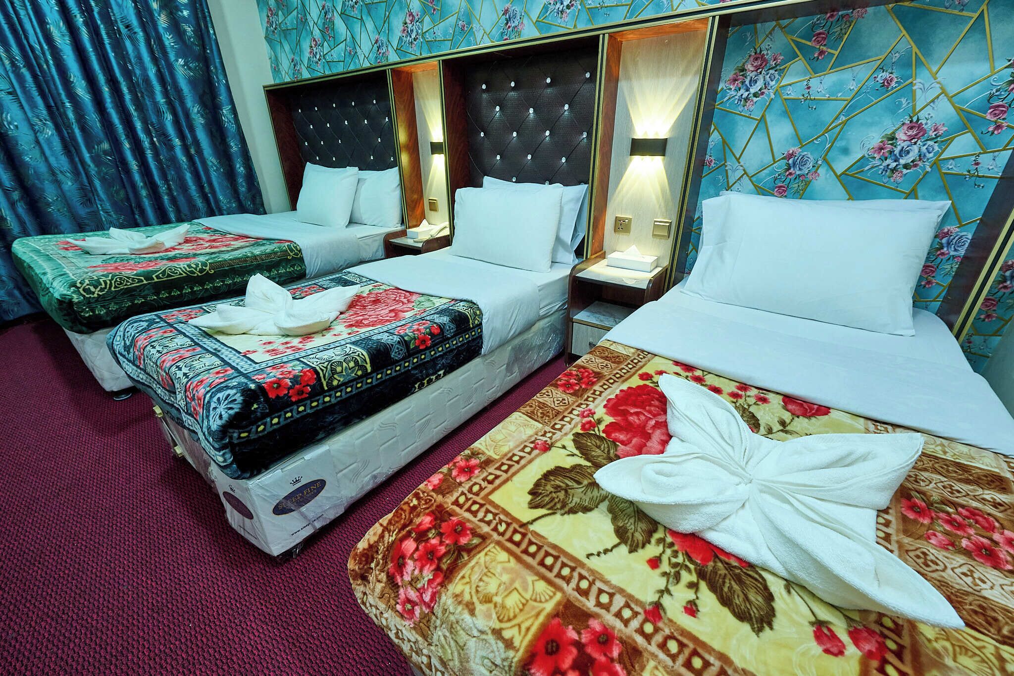 A hotel room with two beds, a large bed with a floral bedspread and a smaller bed with a patterned bedspread.