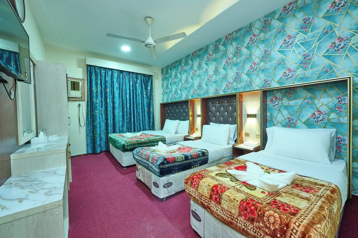A hotel room with two beds, a desk with a mirror, a ceiling fan, and a patterned wall.
