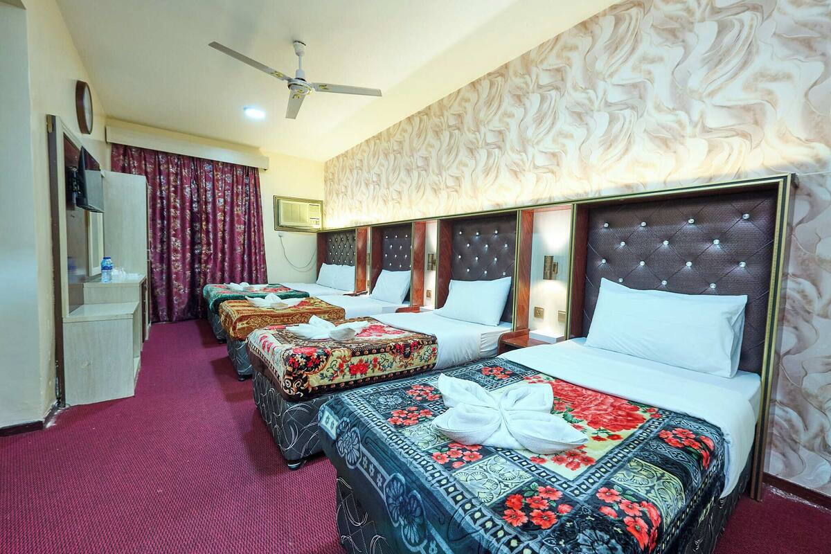 A hotel room with three beds, a ceiling fan, a minibar, and a red carpeted floor.