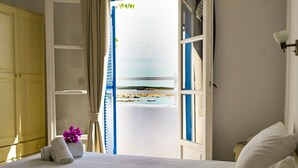 Una habitación de hotel con cama, ventana con vista al mar y balcón con barandilla.