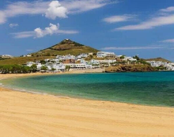 A coastal town with buildings on a hillside overlooking a sandy beach and clear blue waters.