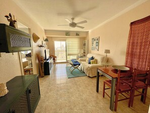Ein Wohnzimmer mit einer Couch, einem Esstisch, Stühlen, einem Deckenventilator und Blick durch eine Glastür.