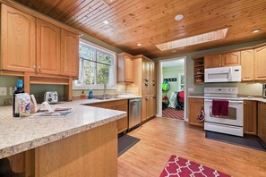 A kitchen with wooden cabinets, a granite countertop, stainless steel appliances, and a red patterned rug. - Whitecaps Cottage | Hot Tub | Near BEACH | AC | PET Friendly (Sauble Beach)