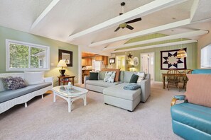 A living room with a sofa, armchair, coffee table, and a dining area with a table and chairs. - Whitecaps Cottage | Hot Tub | Near BEACH | AC | PET Friendly (Sauble Beach)