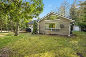 A single-story house with a front yard, a large window, and a visible garage door. - Whitecaps Cottage | Hot Tub | Near BEACH | AC | PET Friendly (Sauble Beach)