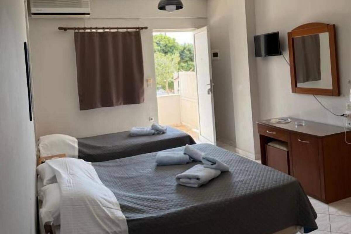 Una habitación con dos camas, un escritorio, un espejo, un televisor y aire acondicionado.