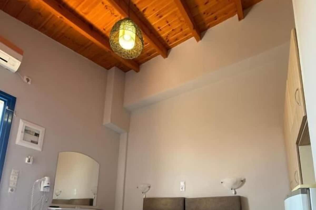 Un dormitorio con techo de madera, una cama con colcha azul, una mesita de noche y una lámpara de pared.