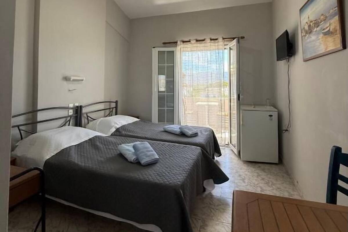 Habitación de hotel con dos camas, una mesita, un televisor y un refrigerador.