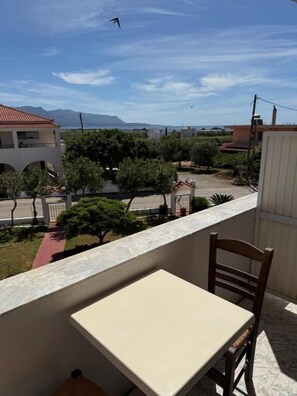 A balcony with a table and chair, overlooking a residential area with houses and trees.