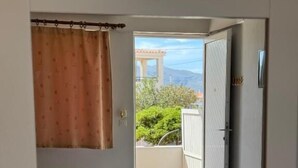 A room with a bed, a bathroom, and a view of a balcony with a door leading outside. - VIAS (Monemvasia)
