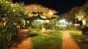 A well-lit courtyard with a pathway leading to a building with multiple balconies. - VIAS (Monemvasia)