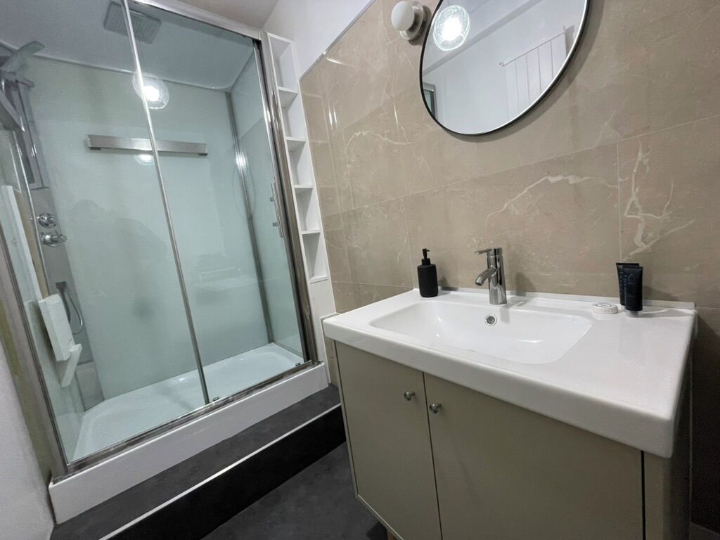 A modern bathroom with a glass-enclosed shower, a white sink with a black soap dispenser, and a mirror above the sink.