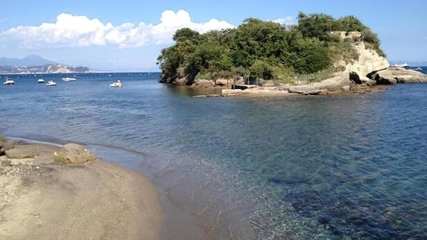 A coastal scene with clear water, a sandy beach, and a rocky island with trees. - Cozy Standard Double Room at B&B Miseno23, 900 m from the sea (Bacoli)