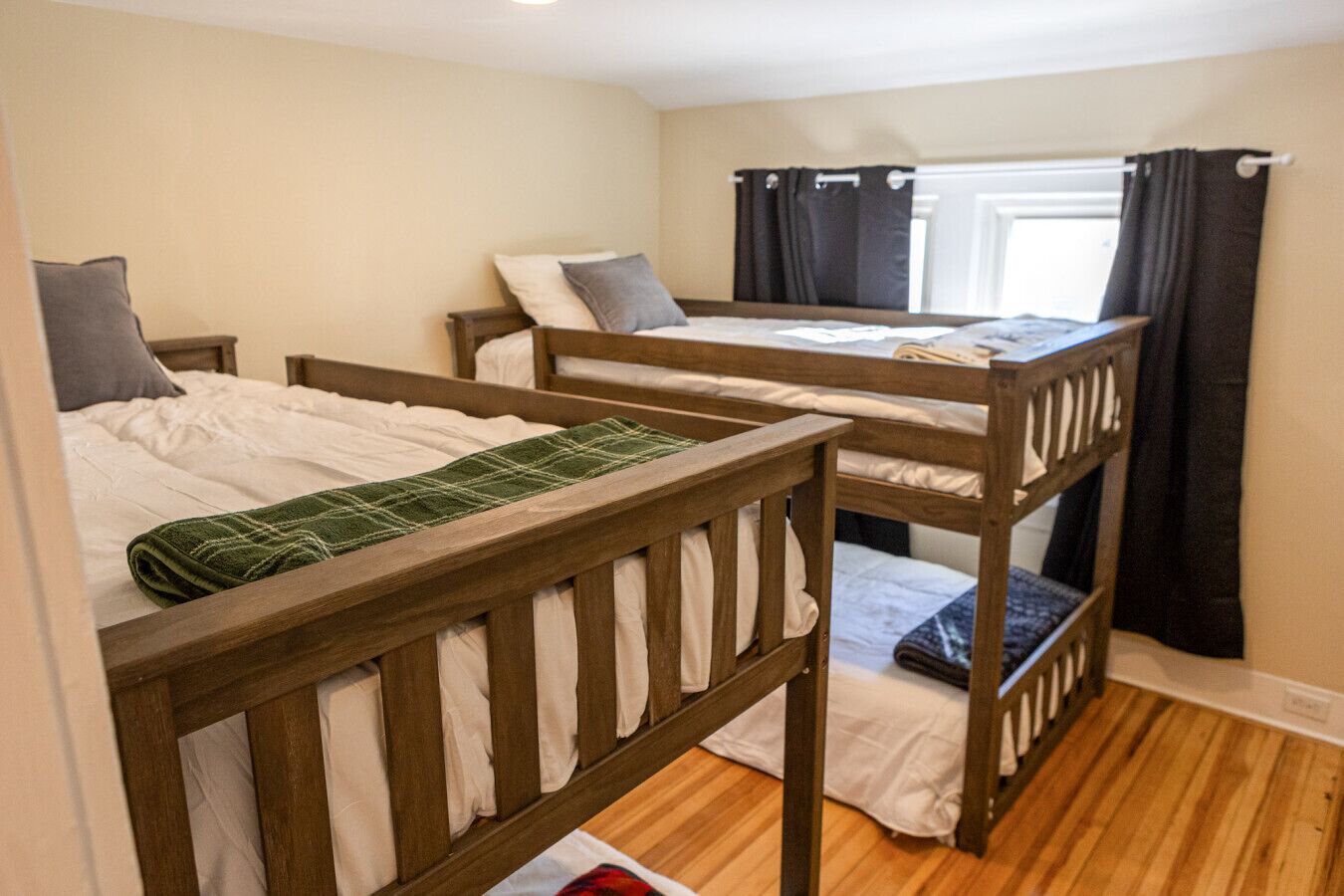Una habitación con tres literas, suelo de madera y una ventana con cortinas.