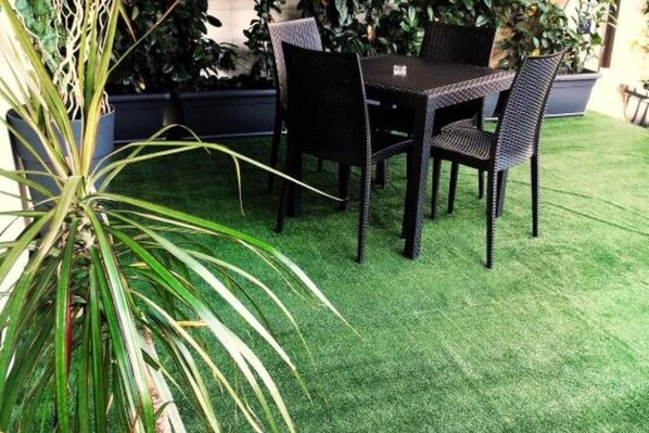 An outdoor patio with a table and chairs, surrounded by potted plants and artificial grass. - B&B Miseno23 - Deluxe Double Room with Terrace and Garden View (Bacoli)