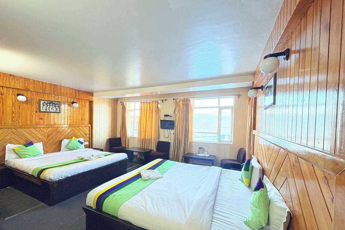Une chambre d’hôtel avec deux lits, un bureau, une chaise, une télévision et une fenêtre avec des rideaux.