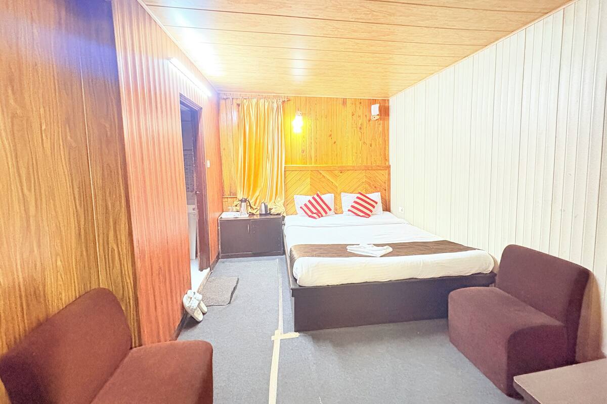 Une chambre d’hôtel de taille réduite, comprenant un lit, deux fauteuils, une petite table et une table de chevet.