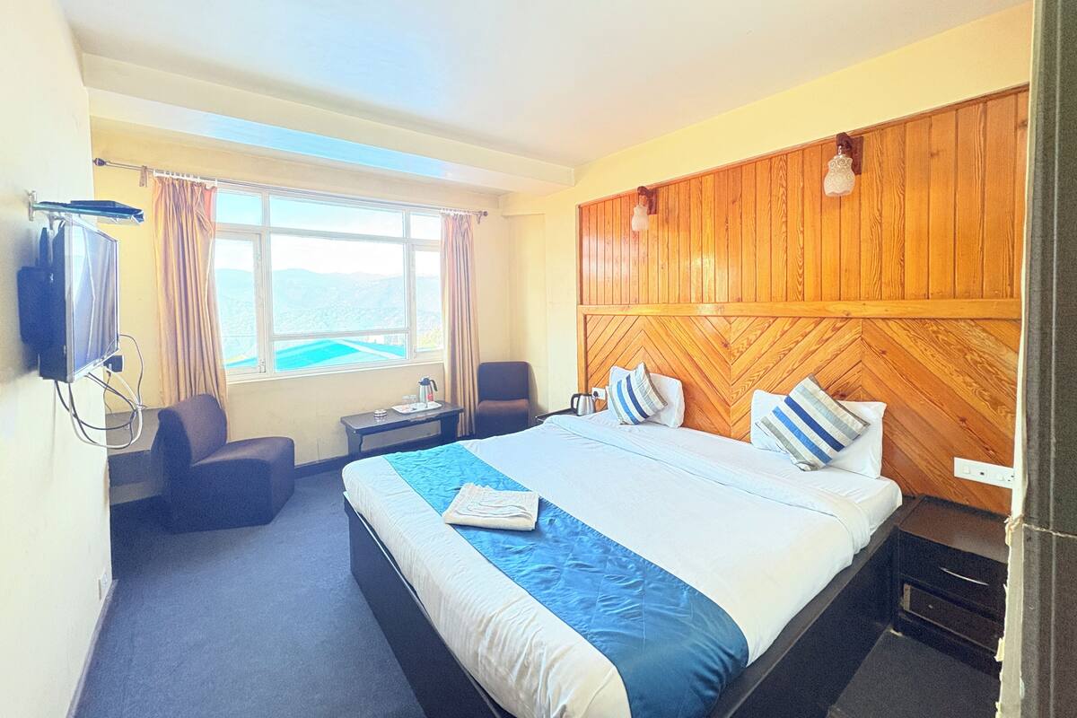Une chambre d’hôtel équipée d’un lit, d’un bureau, d’une chaise, d’une télévision et d’une fenêtre donnant sur un paysage agréable.