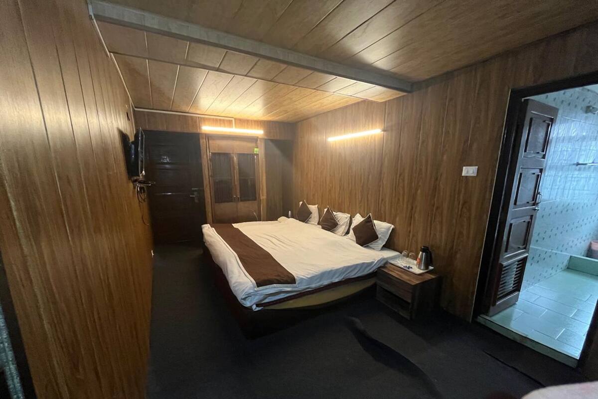 Une chambre d’hôtel avec un grand lit, des murs en bois, une petite table de chevet et une porte donnant sur une salle de bain.
