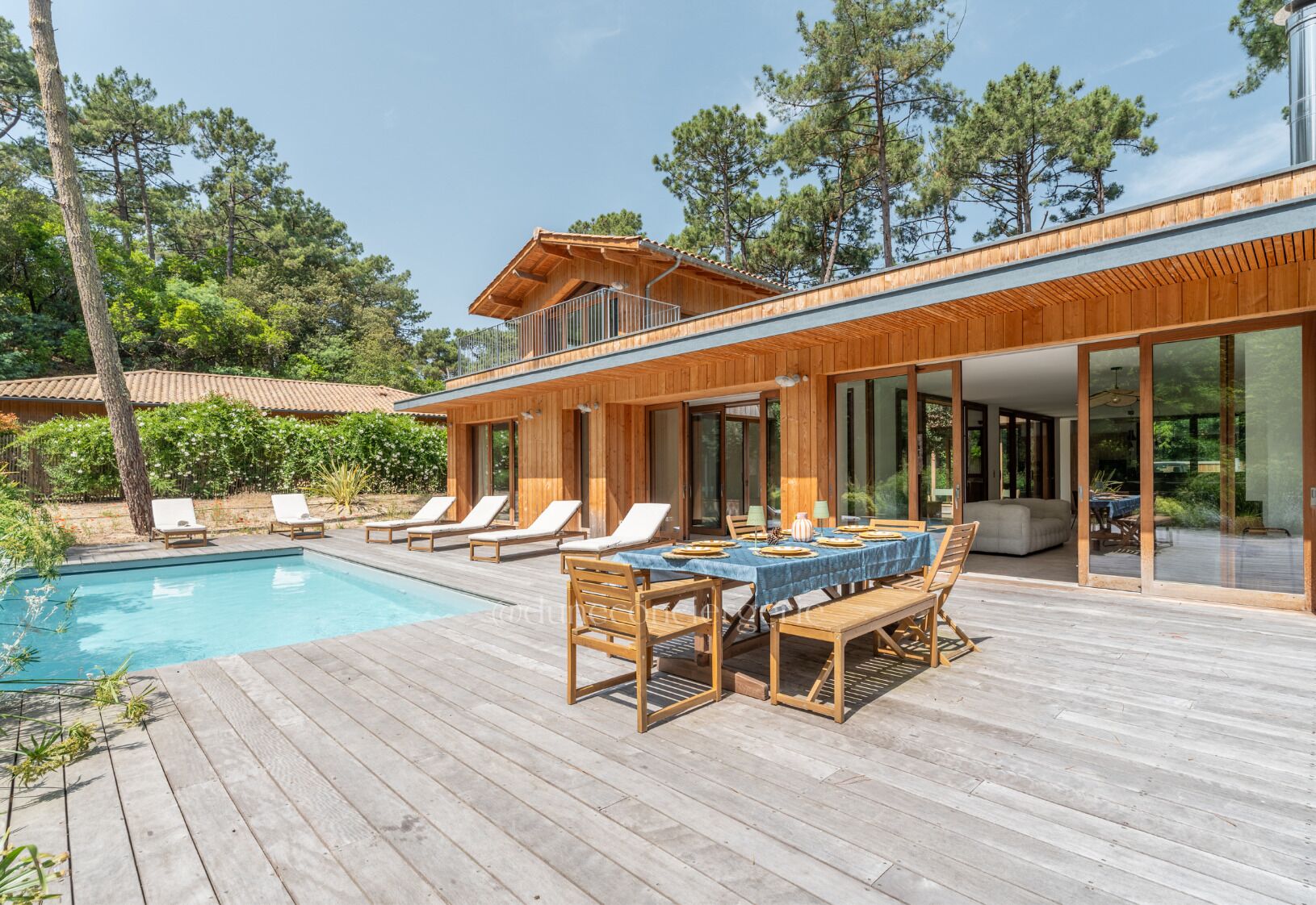 Een modern huis met een zwembad, houten terras en tuinmeubilair.