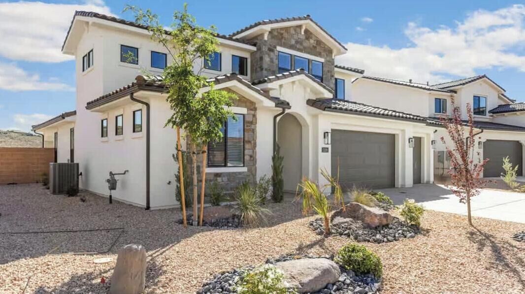 A two-story house with a garage, a landscaped front yard with rocks and plants, and a clear sky.