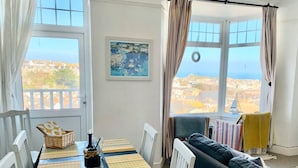 Ein Essbereich mit einem Tisch für zwei Personen, einer Couch und Blick auf die Stadt durch große Fenster.