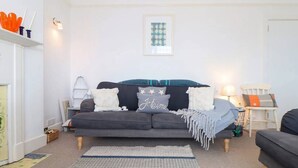 Ein Wohnzimmer mit grauem Sofa, einem gemusterten Teppich und einem gerahmten Kunstwerk an der Wand.